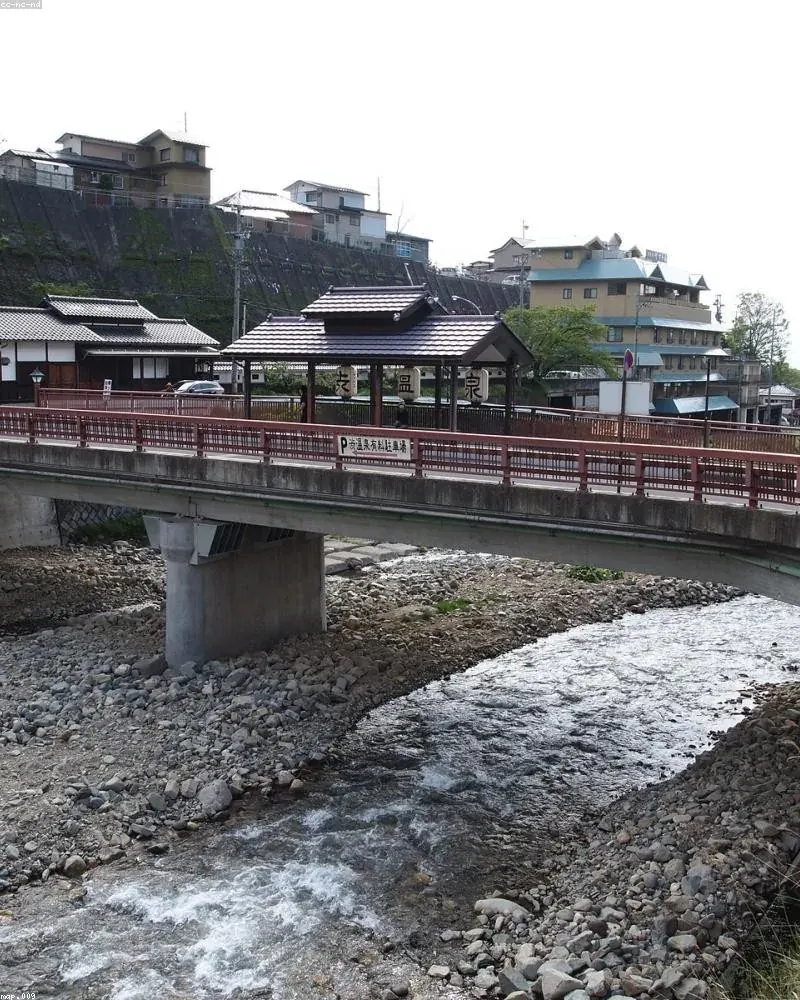 Red bridge over a shallow river in an onsen town, ryokan roofs on the far bank