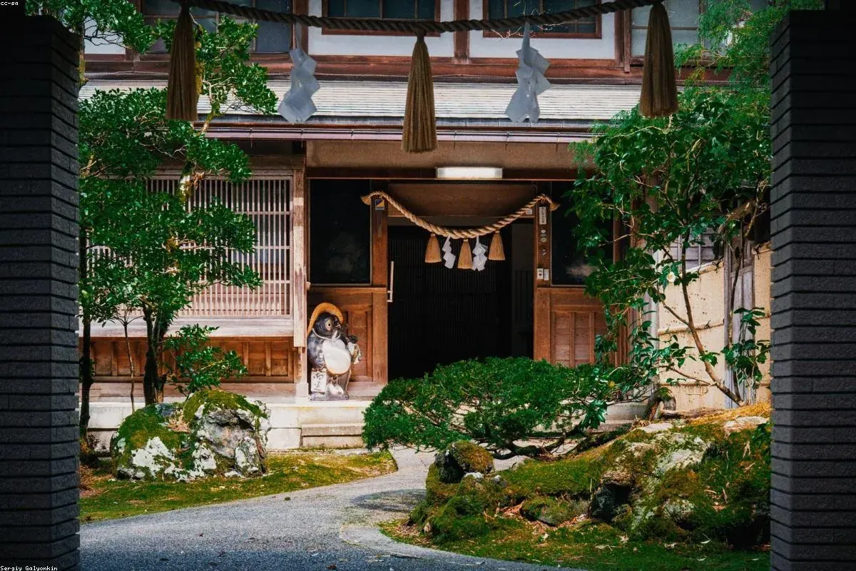 Wooden shrine gate hung with a shimenawa rope, clipped pines in front