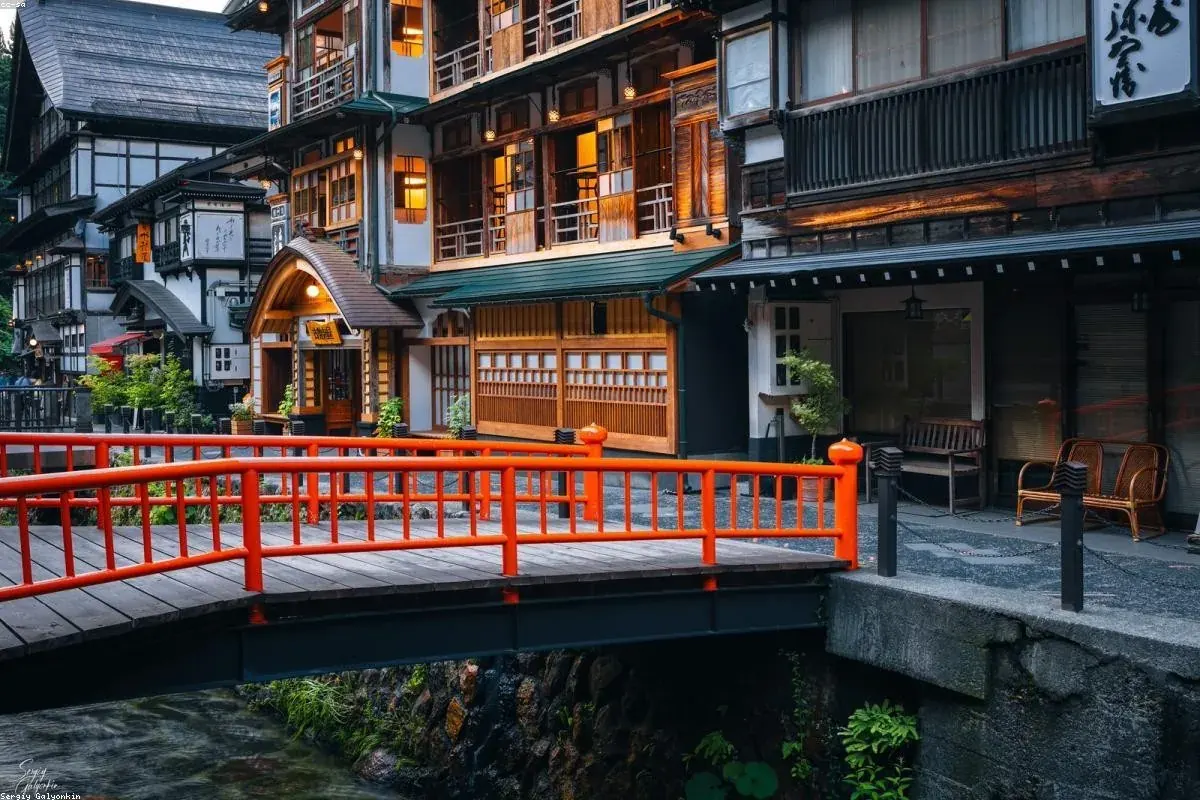 Onsen town street at dusk with a red bridge and lit ryokan facades